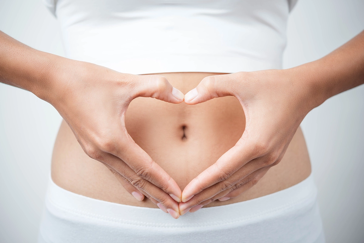 Frau mit Händen die ein Herz vor dem Bauch formen